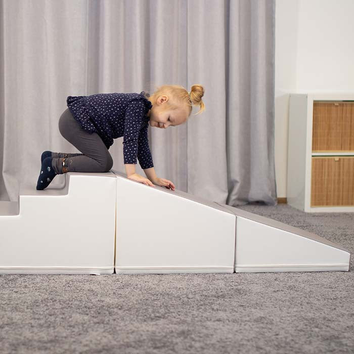 A little girl is engaging in imaginative play on a 4 Piece Soft Play Step and Slide Set - Transformer, made by IGLU Soft Play.